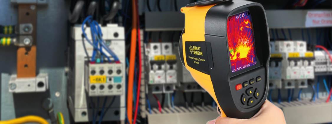 Thermal imaging camera displaying heat patterns while inspecting components inside an industrial electrical cabinet.